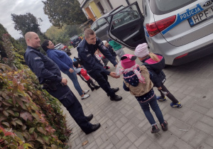 Panowie Policjanci wręczają dzieciom słodkie upominki.